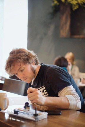 Photo of Artist Artist sitting at a table in a cafe, focusing on a project in front of them, with a coffee mug nearby.